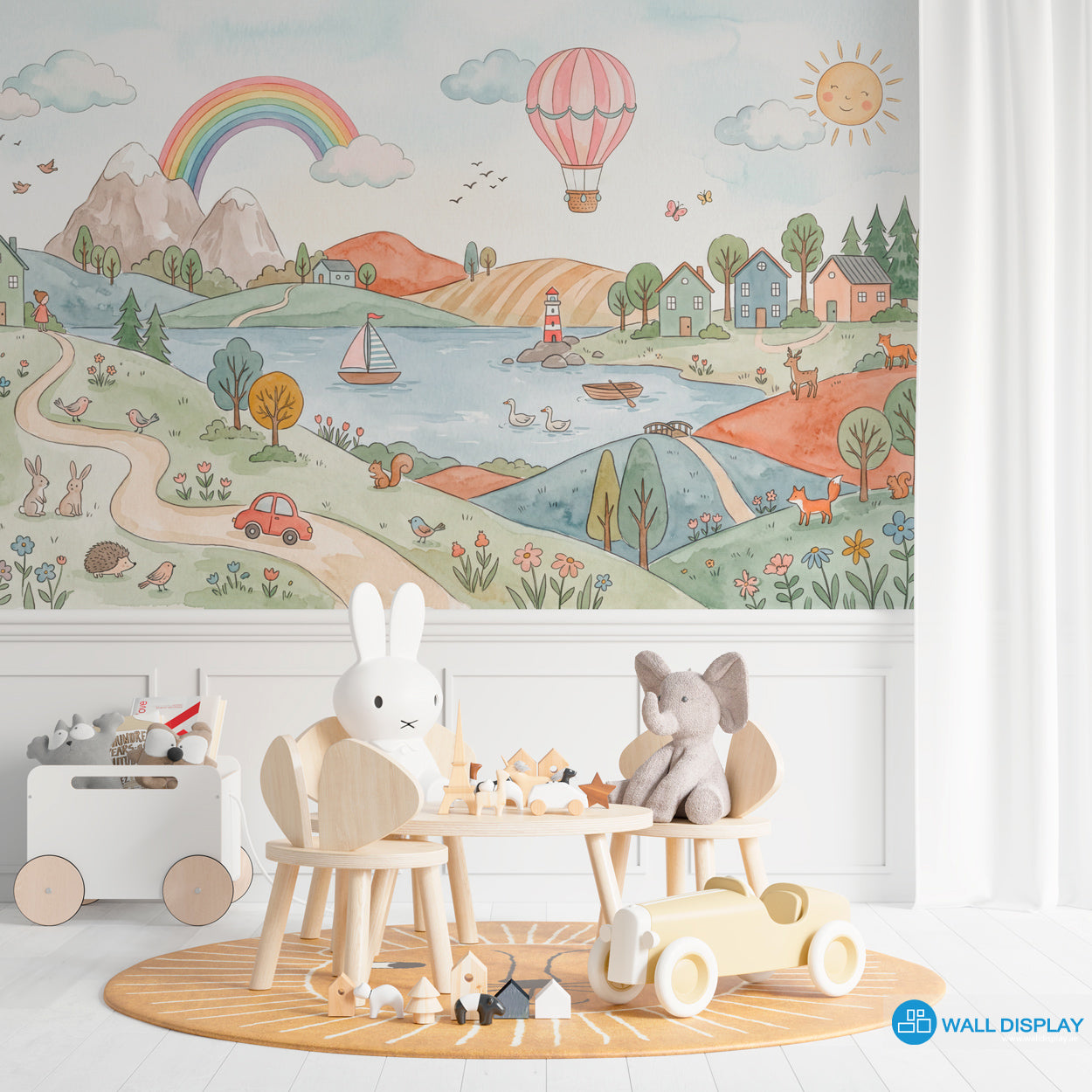 Storybook countryside kids wallpaper mural with pastel hills, rainbow, lake, village houses, hot air balloon, flowers, and woodland animals.